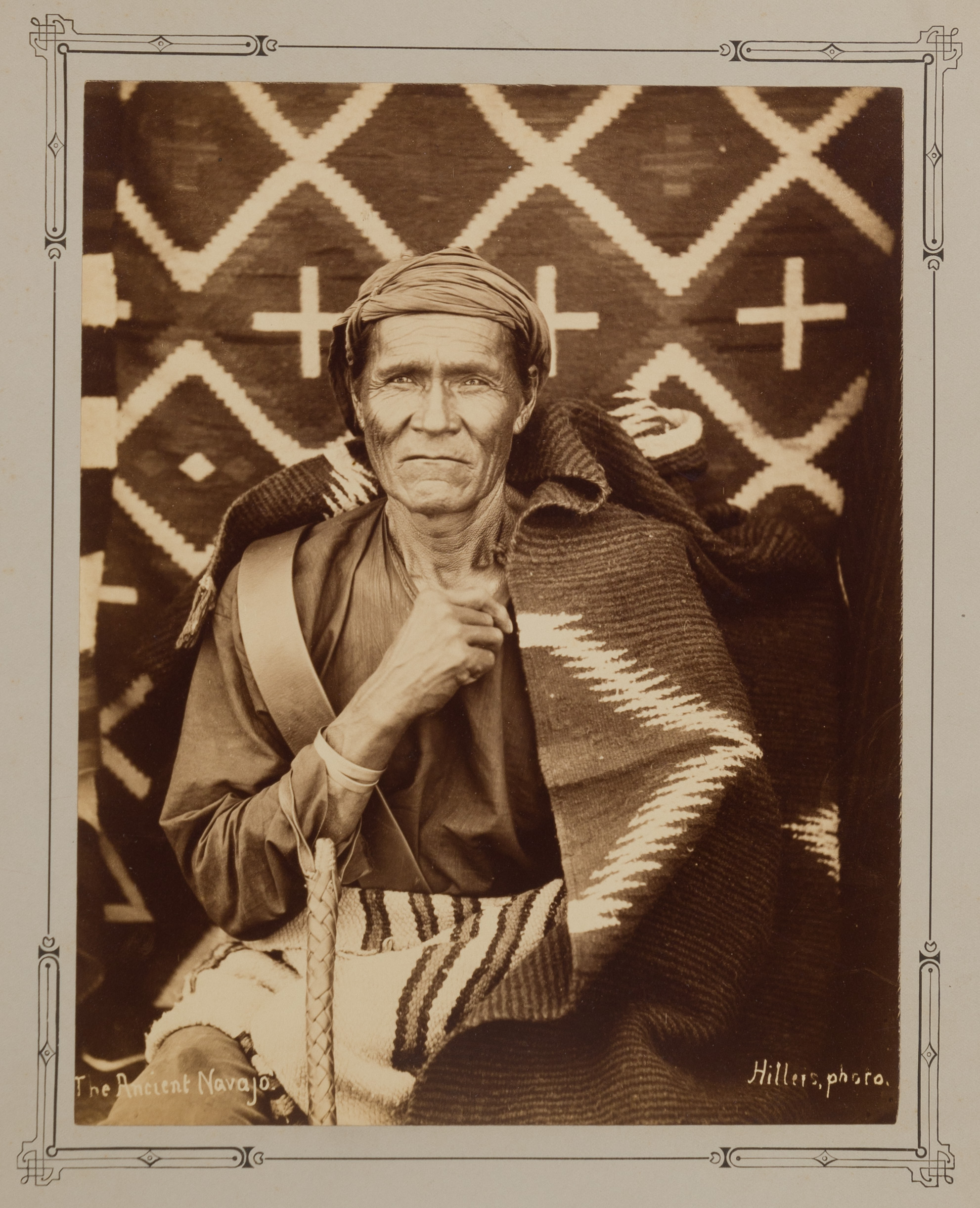 Older person described as Navajo is seated in front of a textile backdrop with geometric designs