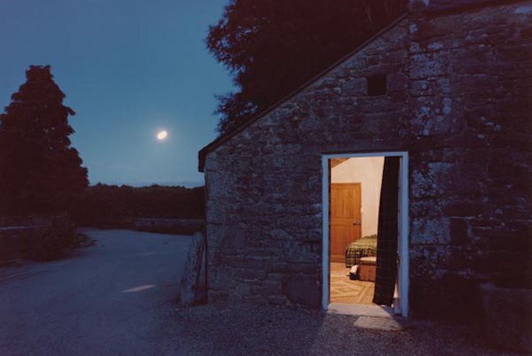 Night time image of house from the outside, dark except for a light seen through the door