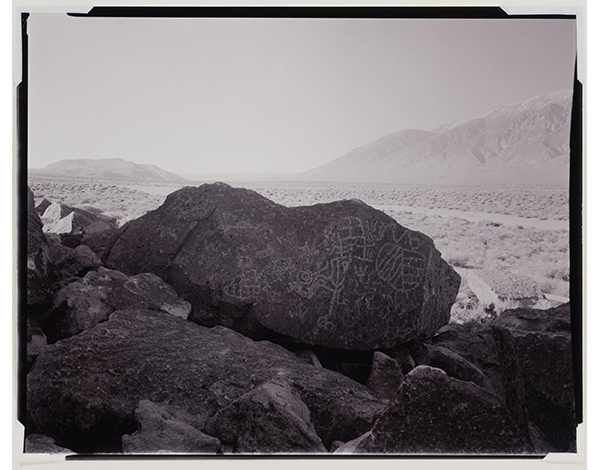 Black and white photograph of a large boulder with petroglyphs carved into it.