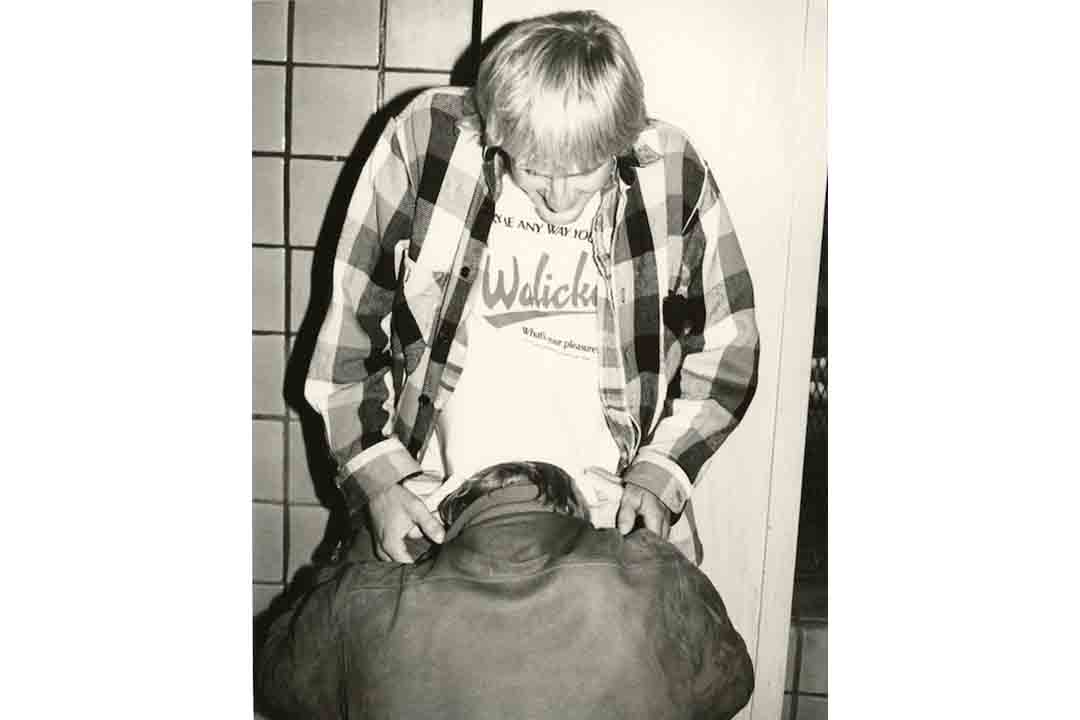 man kneeling in front of other man against a tile wall