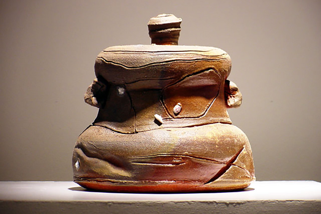Lidded jar with a slightly squat shape and freeform lines carved into its surface.