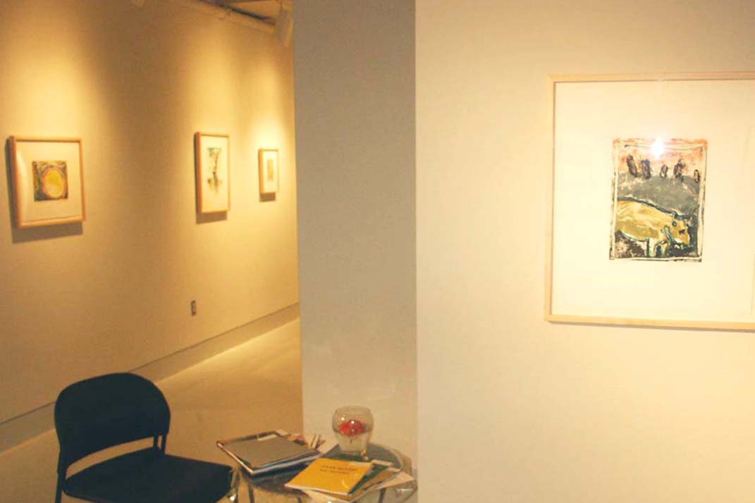 4 colorful prints by Jules Olitski installed in a gallery with a table and chairs in the left foreground