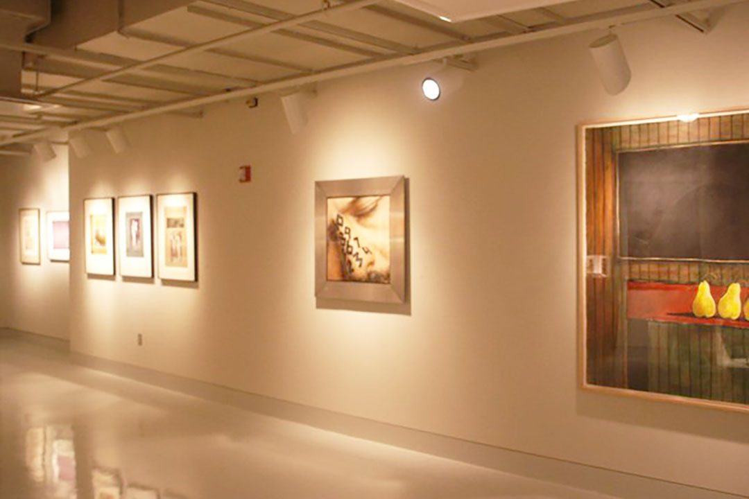 Prints, photographs, and a painting installed along one wall in a gallery