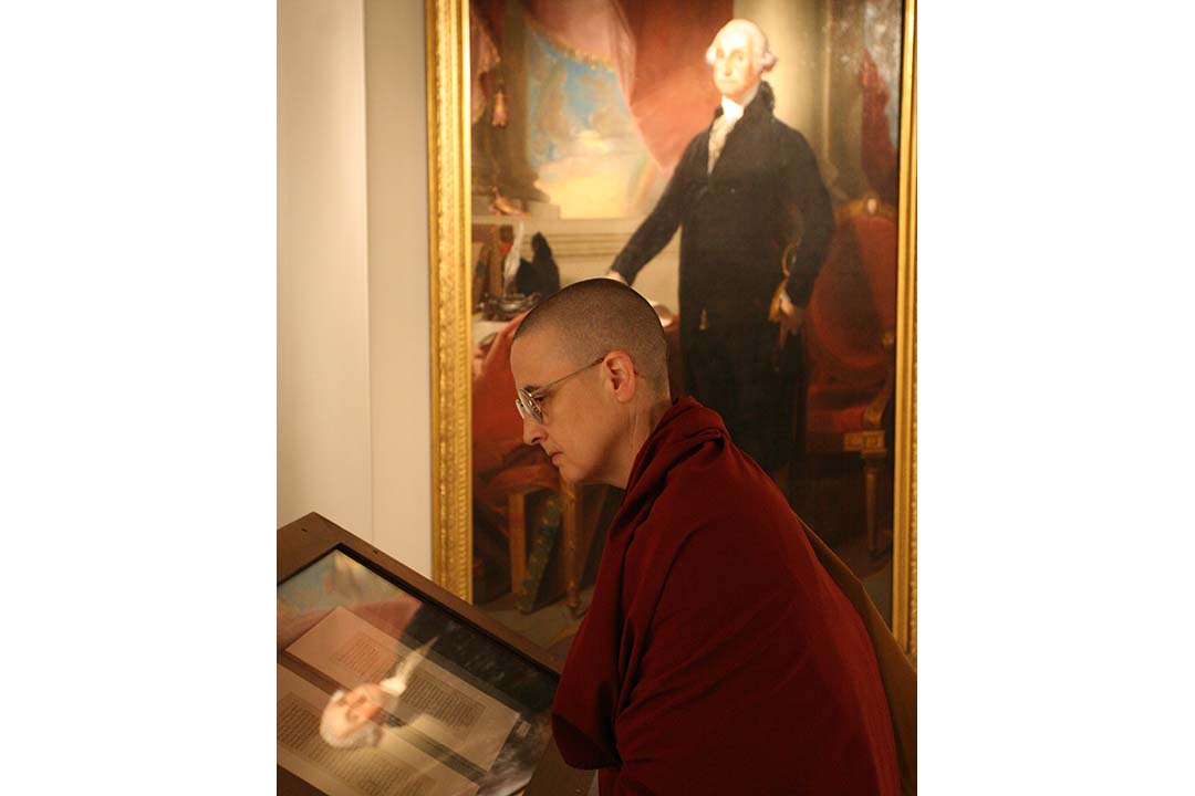 Visitor looks at something in a case with a painting of George Washington behind them.  Washington's face is reflected in glass of display case.